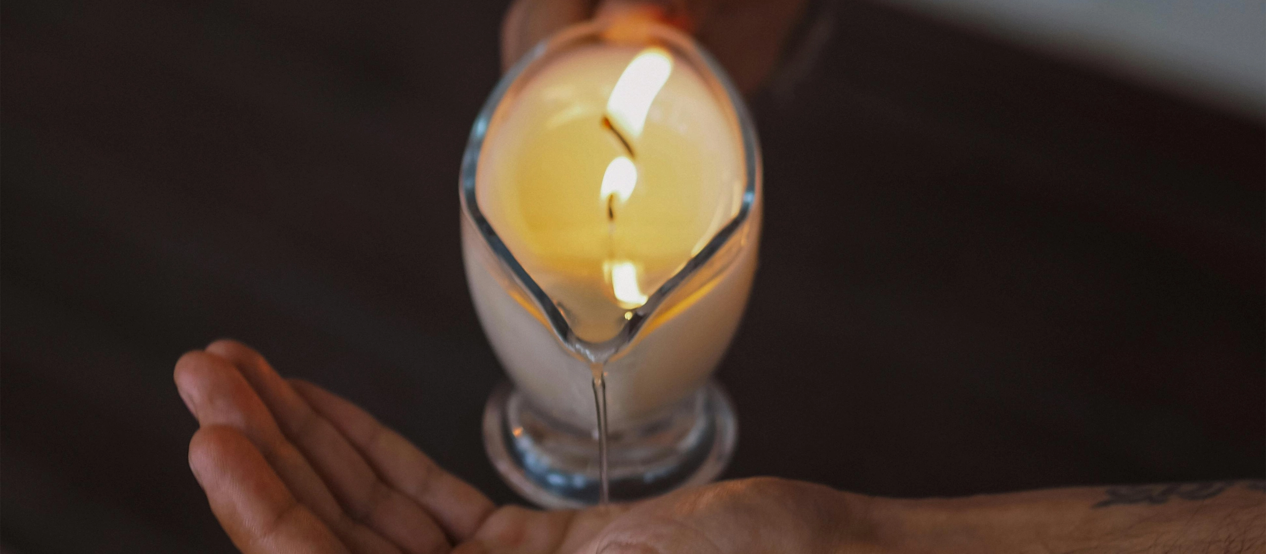 Undistinguishable person pouring an essential oil candle into their hand before starting a massage treatment